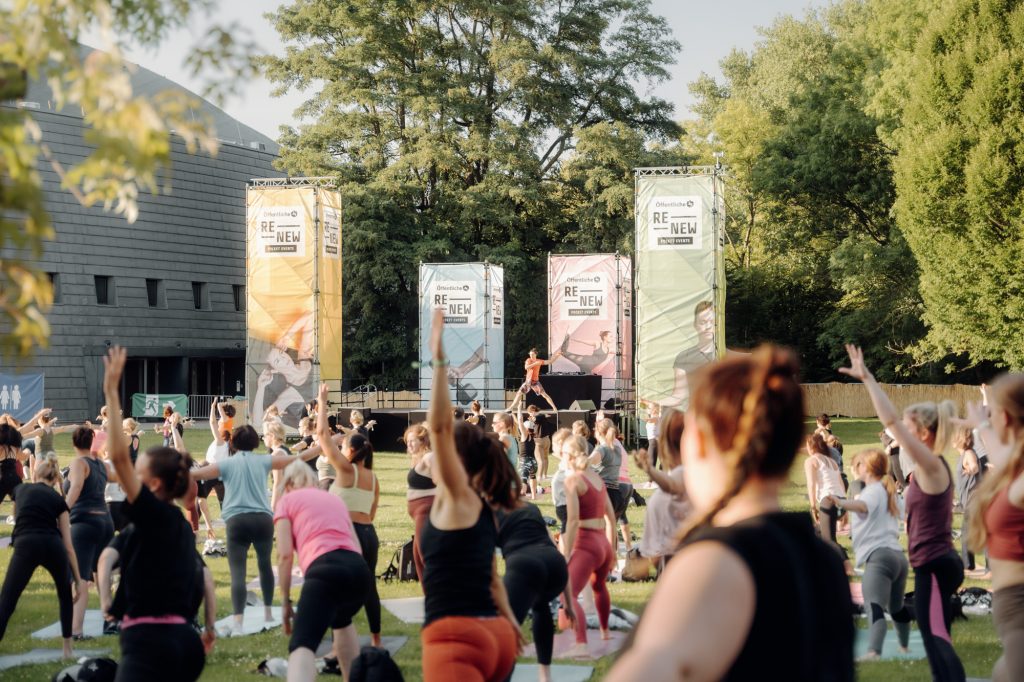 Menschengruppe beim Yoga im Park vor einer Bühne